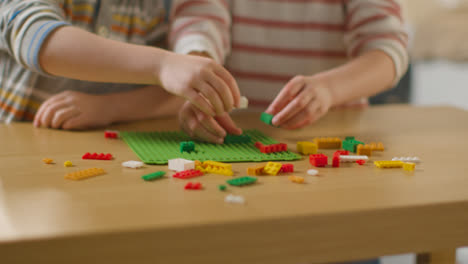 Close-Up-Of-Two-Children-Playing-With-Plastic-Construction-Bricks-On-Table-At-Home-2
